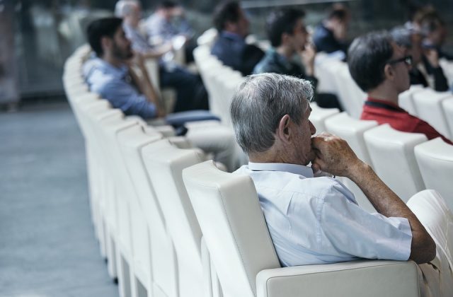 Mężczyźni siedzący na sali konferencyjnej słuchający wykładu