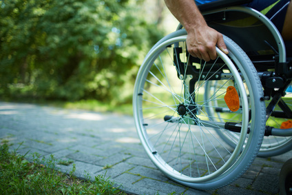 osoba na wózku inwalidzkim jadąca chodnikiem w parku