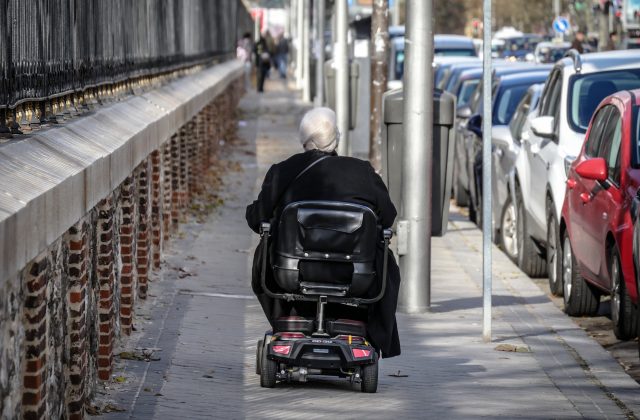 starsza kobieta jadąca chodnikiem na wózku elektrycznym