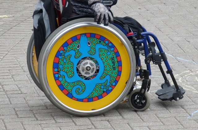 postać siedząca na kolorowym wózku inwalidzkim z ozdobnymi kołami