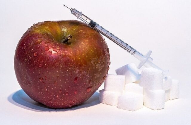 strzykawka oparta na jabłku, obok znajdują się kostki cukru