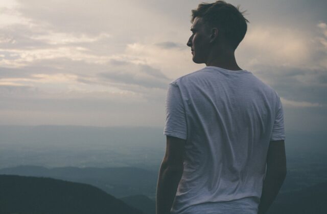 Młody mężczyzna stojący tyłem na szczycie wzgórza i patrzący w dal