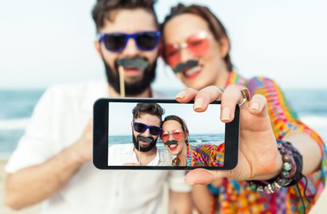 Para trzymająca sztuczne wąsy i robiąca selfie