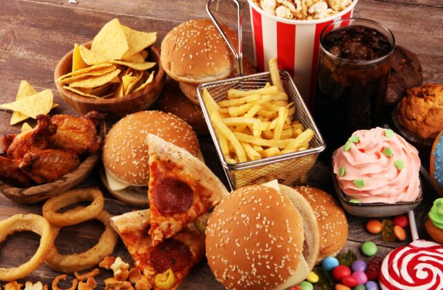Fast food i produkty wysoko przetworzone – burgery, frytki, pizza, chipsy i słodycze na stole